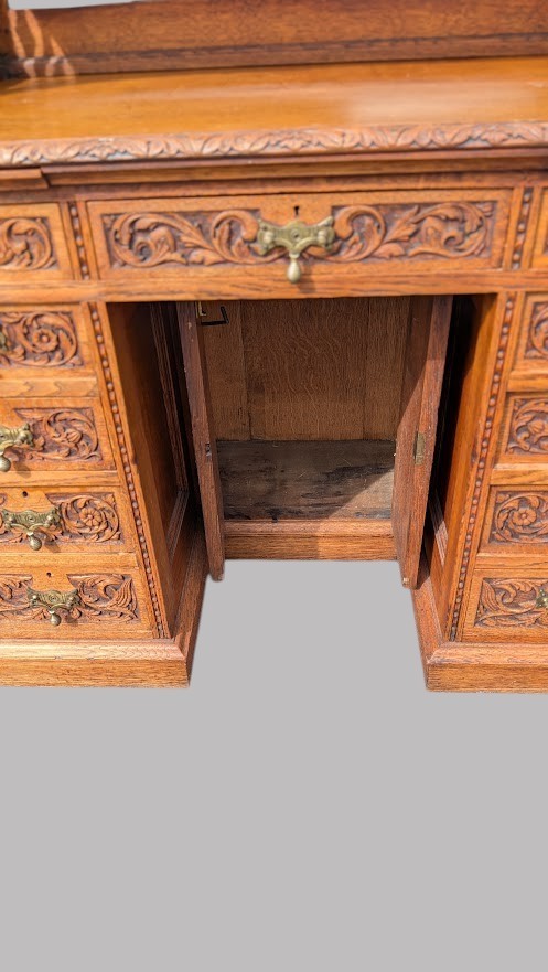 A late Victorian quarter-sawn oak collectors desk featuring carved pedestals, multiple shallow drawer tiers, a central cupboard, and a top spindle gallery. View XI