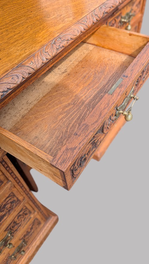 A late Victorian quarter-sawn oak collectors desk featuring carved pedestals, multiple shallow drawer tiers, a central cupboard, and a top spindle gallery. View XII