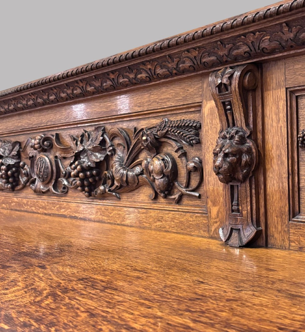 A carved dark oak Victorian sideboard featuring a raised back gallery, relief fruit carvings, barley twist columns, and two pedestal cupboards flanking an open centre. View IV