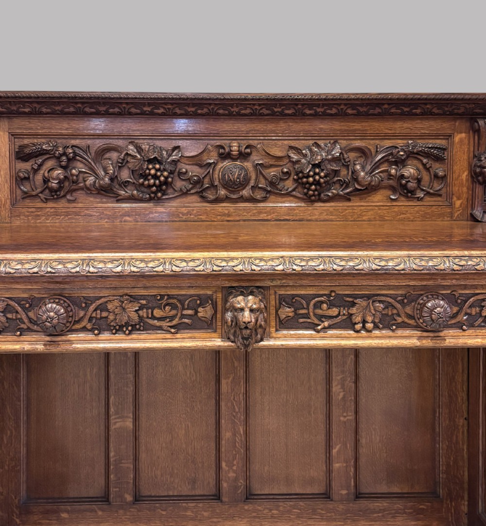 A carved dark oak Victorian sideboard featuring a raised back gallery, relief fruit carvings, barley twist columns, and two pedestal cupboards flanking an open centre. View V