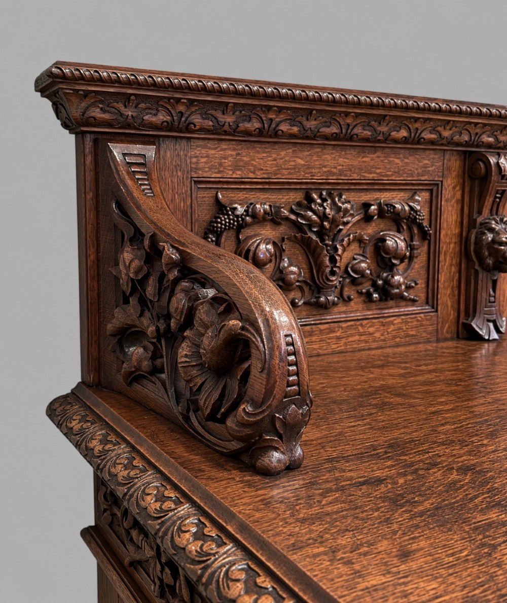 A carved dark oak Victorian sideboard featuring a raised back gallery, relief fruit carvings, barley twist columns, and two pedestal cupboards flanking an open centre. View VI
