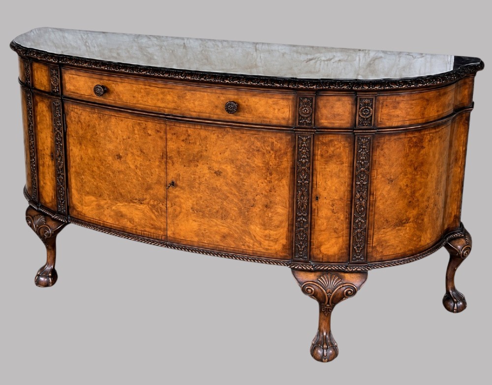 A bow-front burr walnut sideboard with carved pilasters, twin cupboard doors, a top drawer, and four carved cabriole legs ending in ball and claw feet. View VI