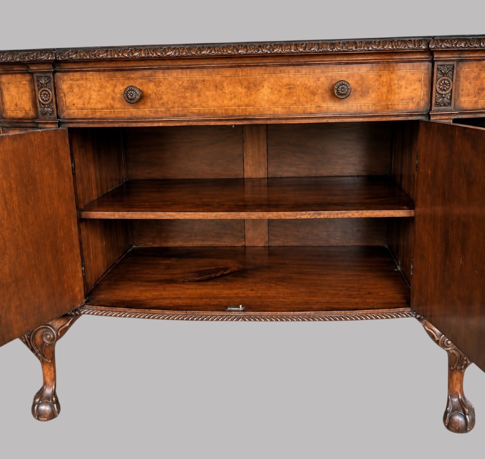 A bow-front burr walnut sideboard with carved pilasters, twin cupboard doors, a top drawer, and four carved cabriole legs ending in ball and claw feet. View VII
