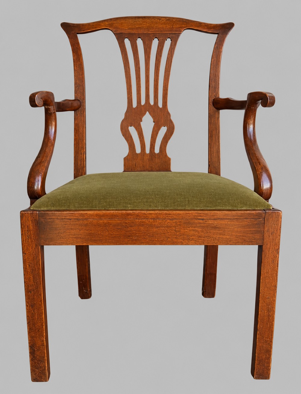 A Georgian Chippendale style mahogany elbow chair with a pierced splat back, shaped arms, and a green velvet seat.