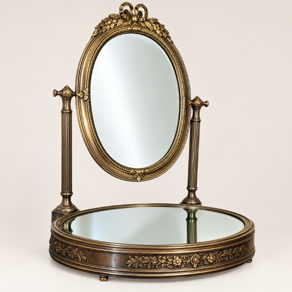An antique late 19th-century French brass vanity mirror featuring an oval pivoting glass frame adorned with a bow crest, supported by two fluted columns resting on a circular mirrored base. View II