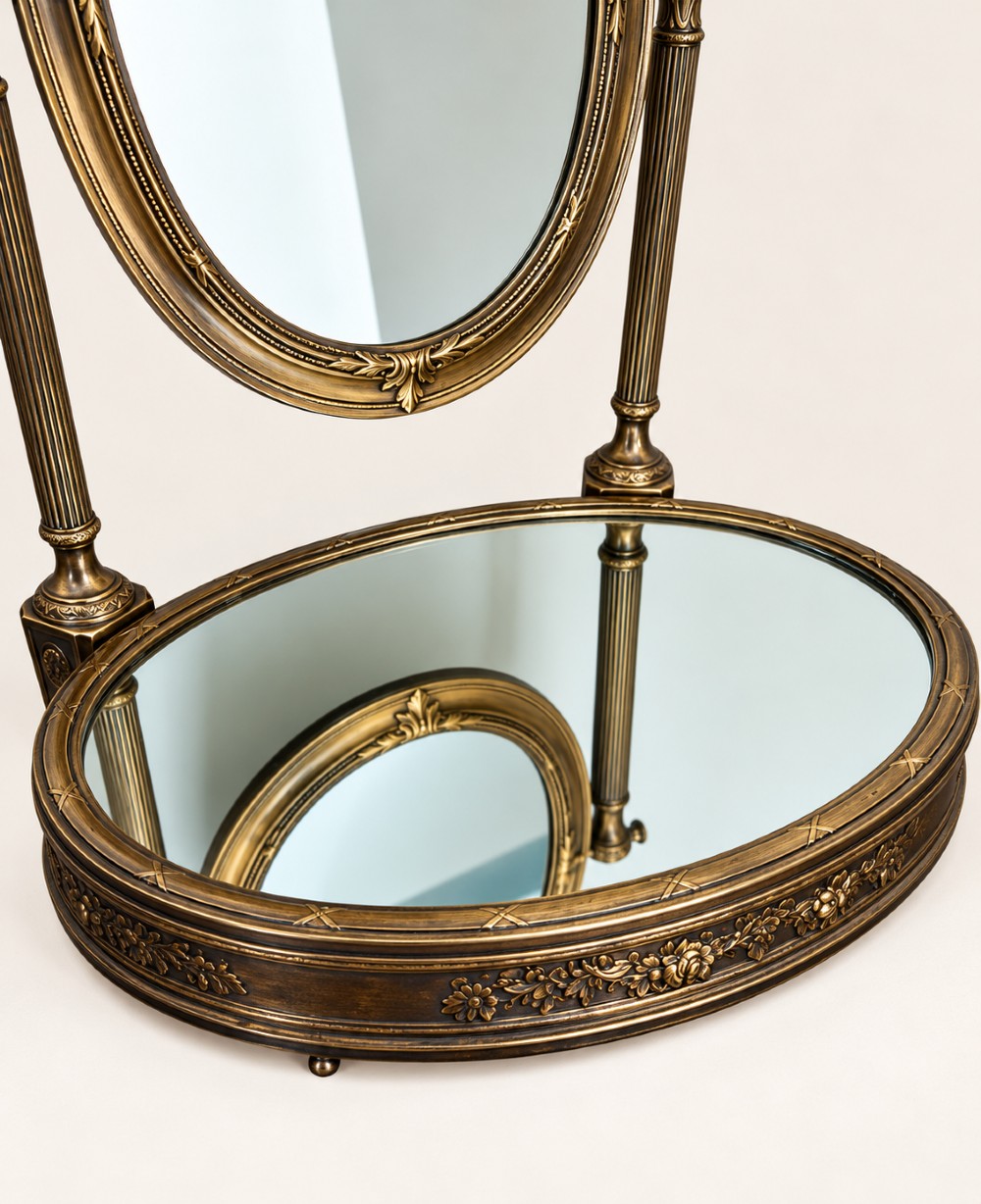 An antique late 19th-century French brass vanity mirror featuring an oval pivoting glass frame adorned with a bow crest, supported by two fluted columns resting on a circular mirrored base. View V