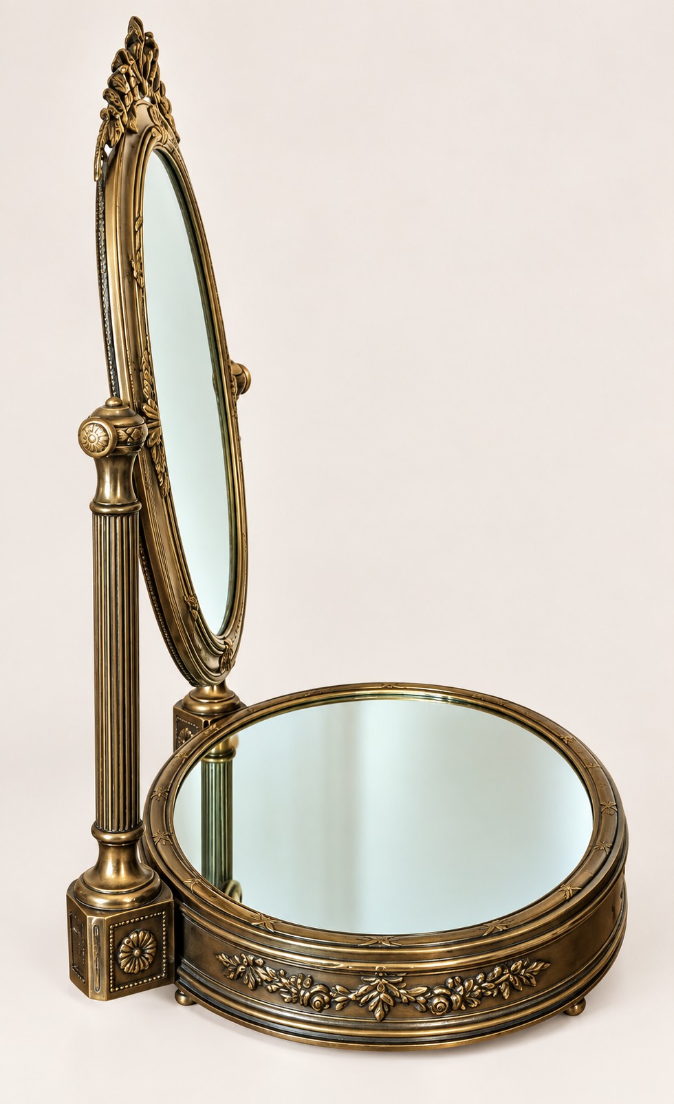 An antique late 19th-century French brass vanity mirror featuring an oval pivoting glass frame adorned with a bow crest, supported by two fluted columns resting on a circular mirrored base. View VI