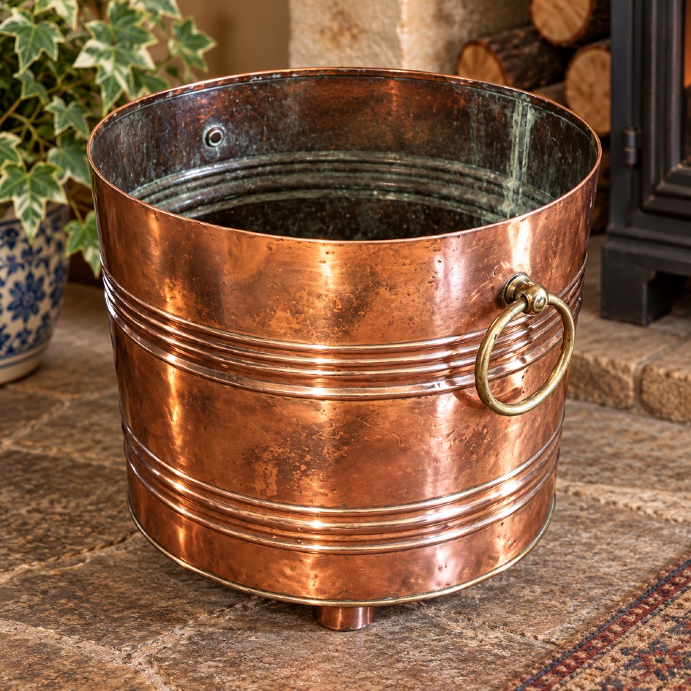 A cylindrical Victorian copper log bin featuring raised horizontal ribs, brass drop ring handles, and short metal feet. View II