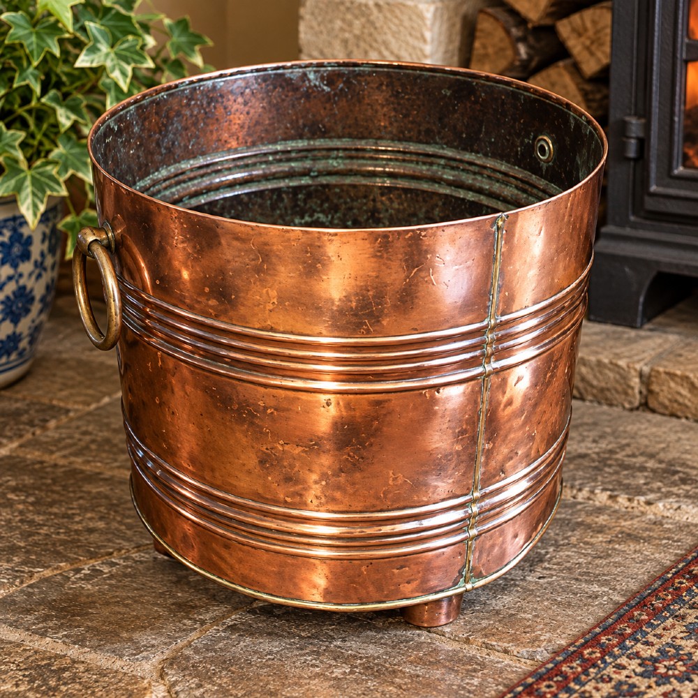 A cylindrical Victorian copper log bin featuring raised horizontal ribs, brass drop ring handles, and short metal feet. View III