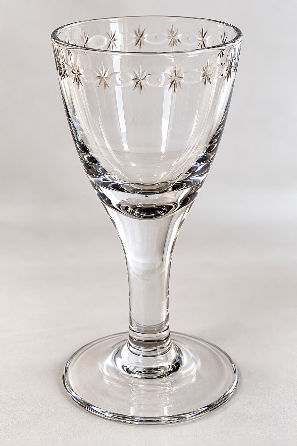 An antique clear lead glass dram glass featuring a flared rim with wheel-engraved starburst motifs, a solid thick stem, and a flat circular foot. View II