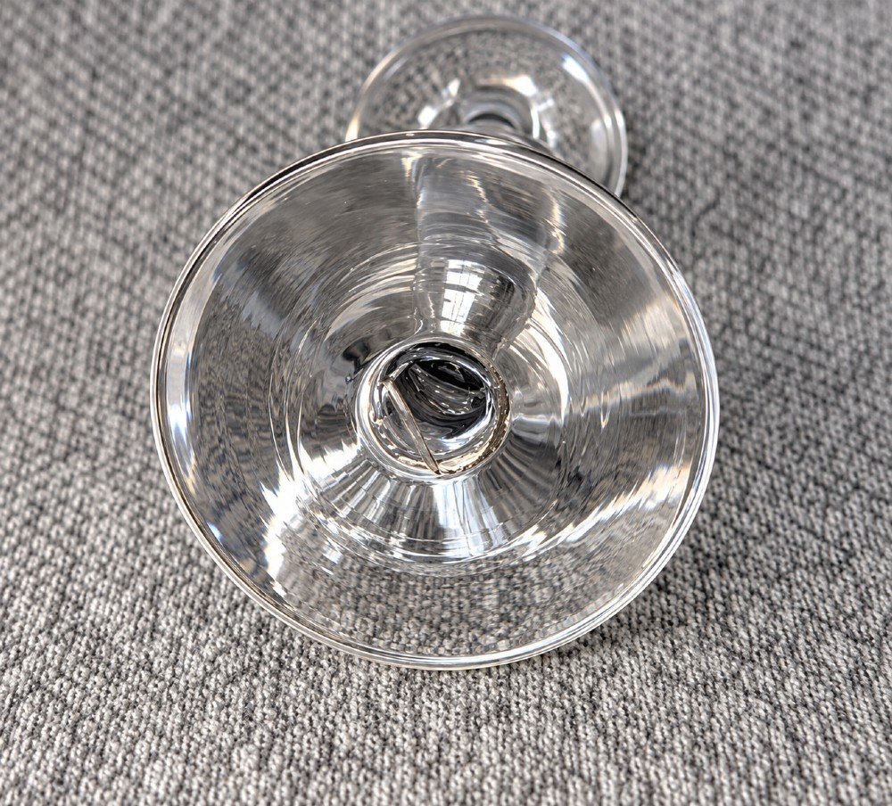 An antique clear lead glass dram glass featuring a flared rim with wheel-engraved starburst motifs, a solid thick stem, and a flat circular foot. View IV