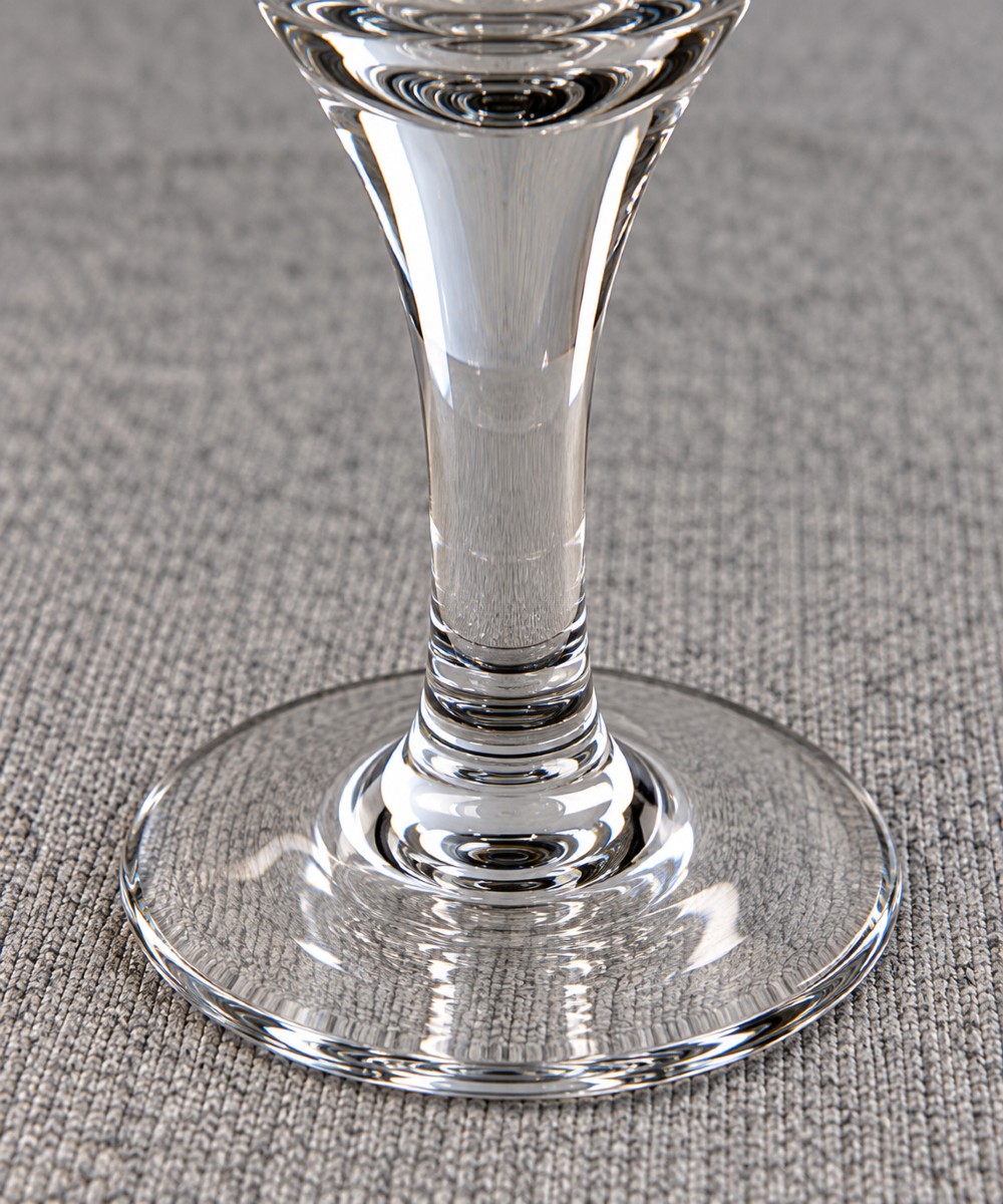 An antique clear lead glass dram glass featuring a flared rim with wheel-engraved starburst motifs, a solid thick stem, and a flat circular foot. View V
