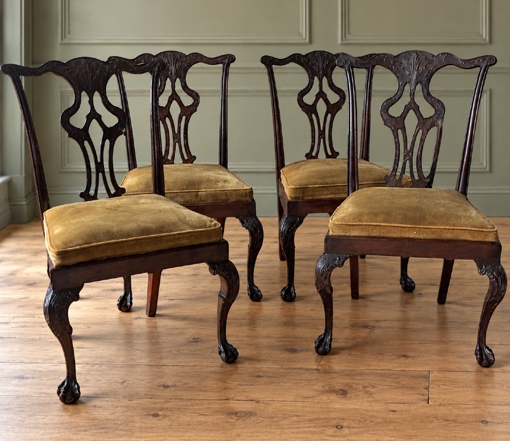 A set of four mahogany Chippendale style dining chairs featuring carved pierced splats, gold-coloured velvet seats, and cabriole front legs with ball-and-claw feet.