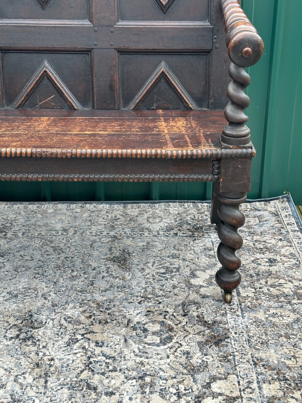 A dark oak 19th-century settle featuring a four-panel back with geometric diamond moulding, barley twist supports, and small brass castors. View III