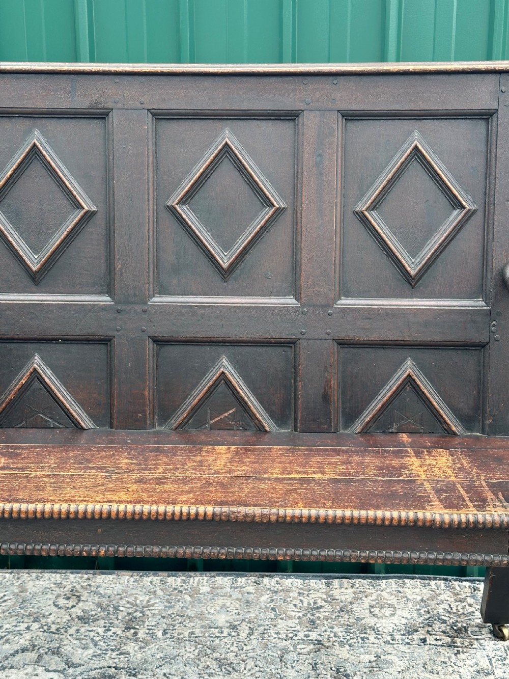 A dark oak 19th-century settle featuring a four-panel back with geometric diamond moulding, barley twist supports, and small brass castors. View IV