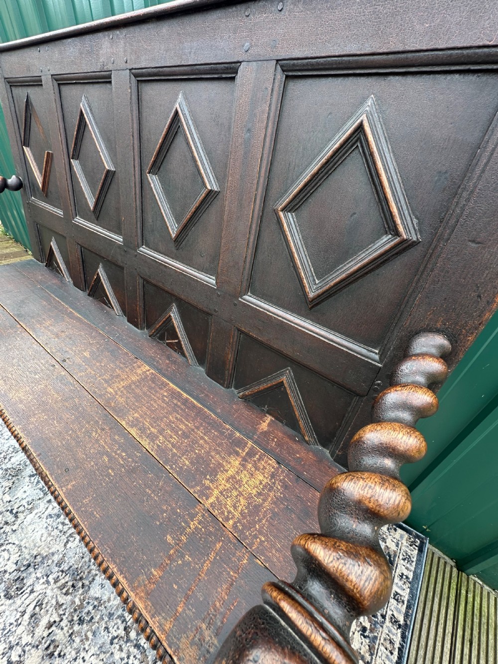 A dark oak 19th-century settle featuring a four-panel back with geometric diamond moulding, barley twist supports, and small brass castors. View VII