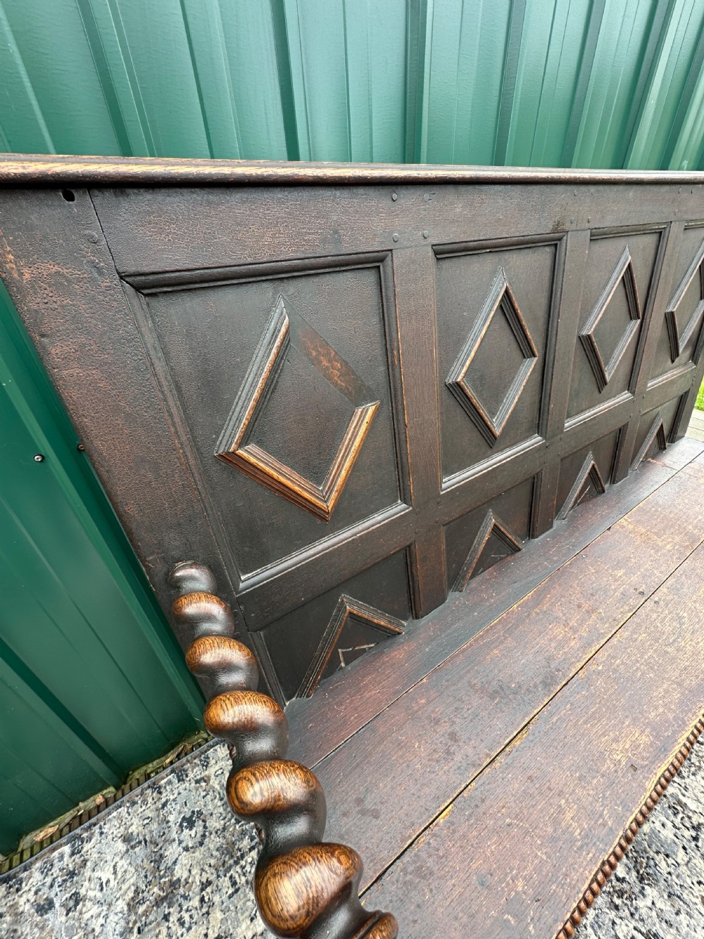 A dark oak 19th-century settle featuring a four-panel back with geometric diamond moulding, barley twist supports, and small brass castors. View X