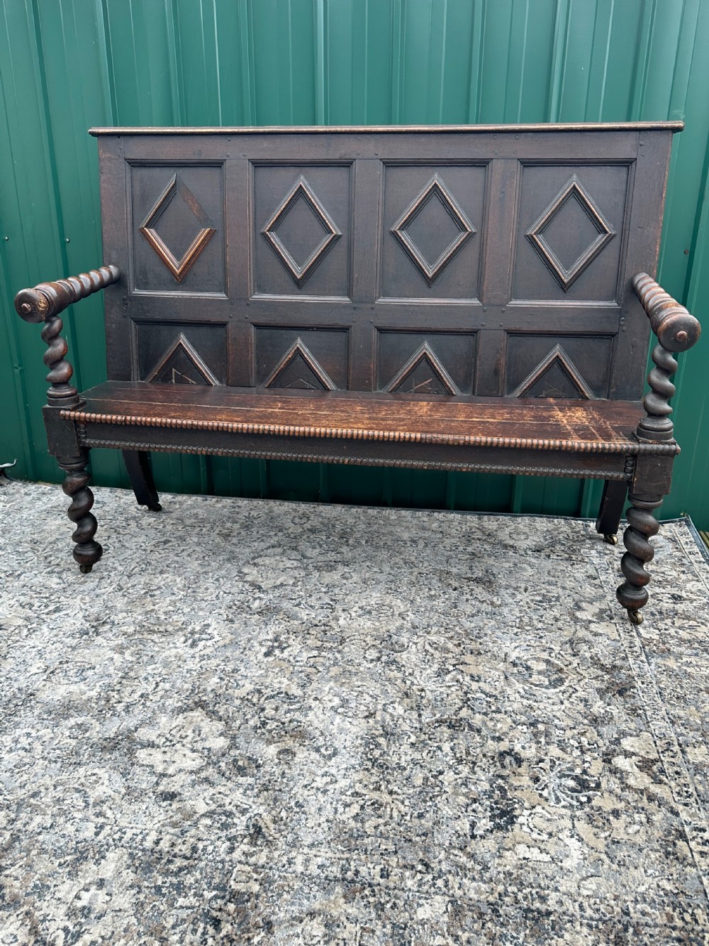 A dark oak 19th-century settle featuring a four-panel back with geometric diamond moulding, barley twist supports, and small brass castors. View XII