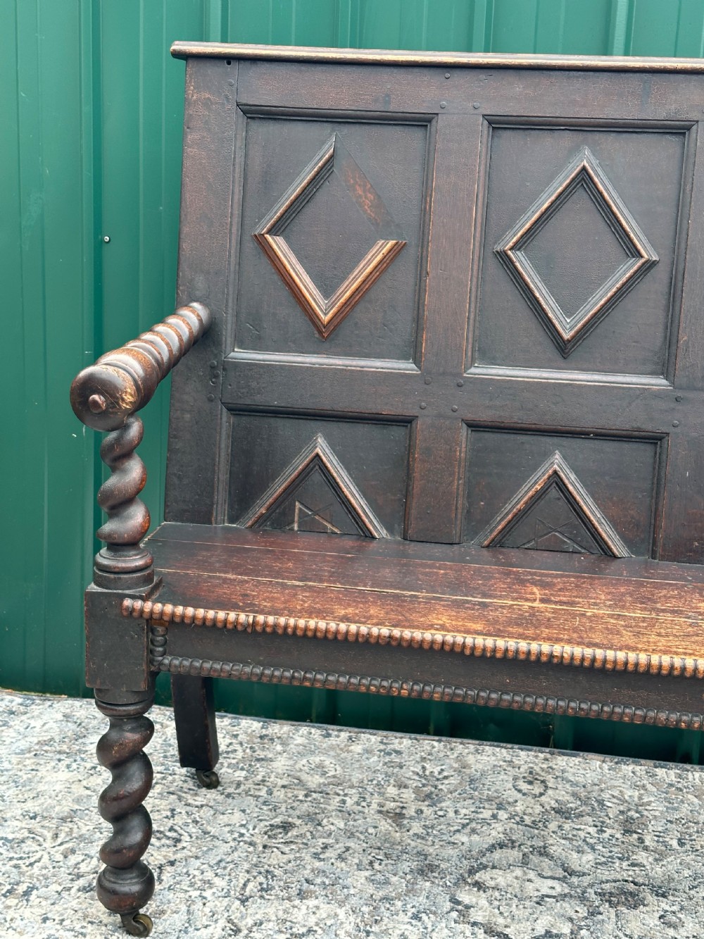 A dark oak 19th-century settle featuring a four-panel back with geometric diamond moulding, barley twist supports, and small brass castors. View XIV