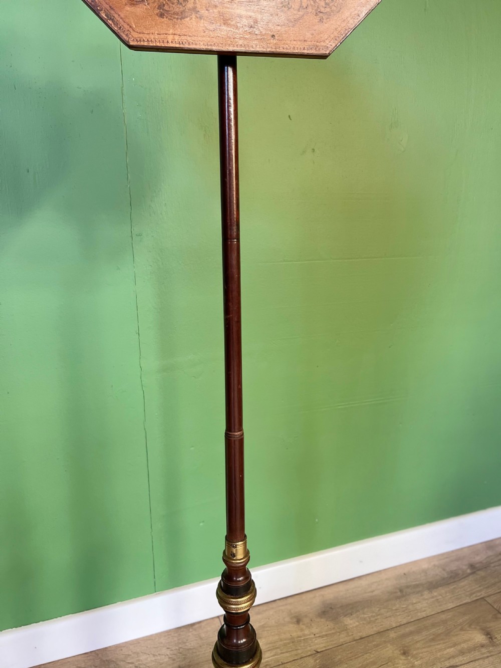 An antique Regency pole fire screen featuring an octagonal pokerwork panel supported on a turned wooden column with a plinth base resting on brass claw feet. View IV