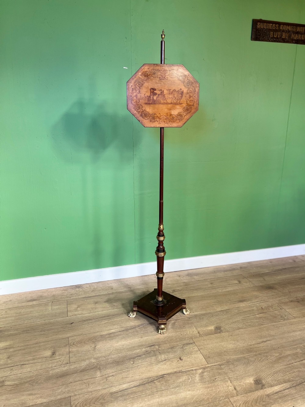 An antique Regency pole fire screen featuring an octagonal pokerwork panel supported on a turned wooden column with a plinth base resting on brass claw feet.