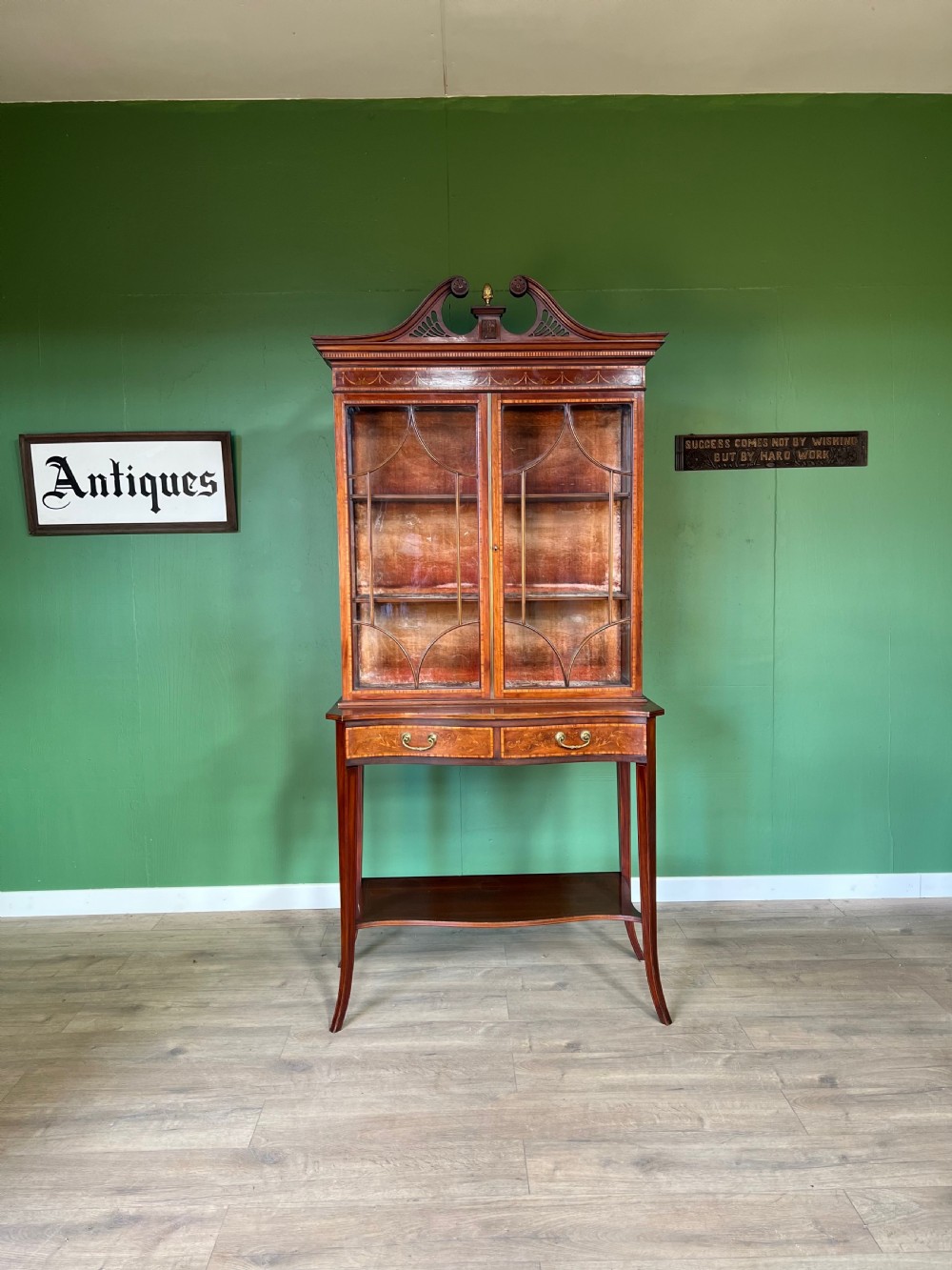 An Edwardian Sheraton Revival inlaid mahogany display cabinet featuring a swan-neck pediment, astragal glazed doors, drawers, and tapered legs.