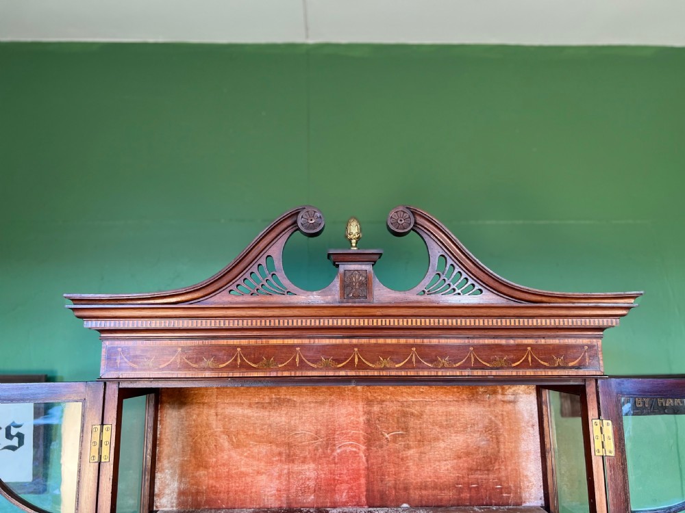 An Edwardian Sheraton Revival inlaid mahogany display cabinet featuring a swan-neck pediment, astragal glazed doors, drawers, and tapered legs. View III