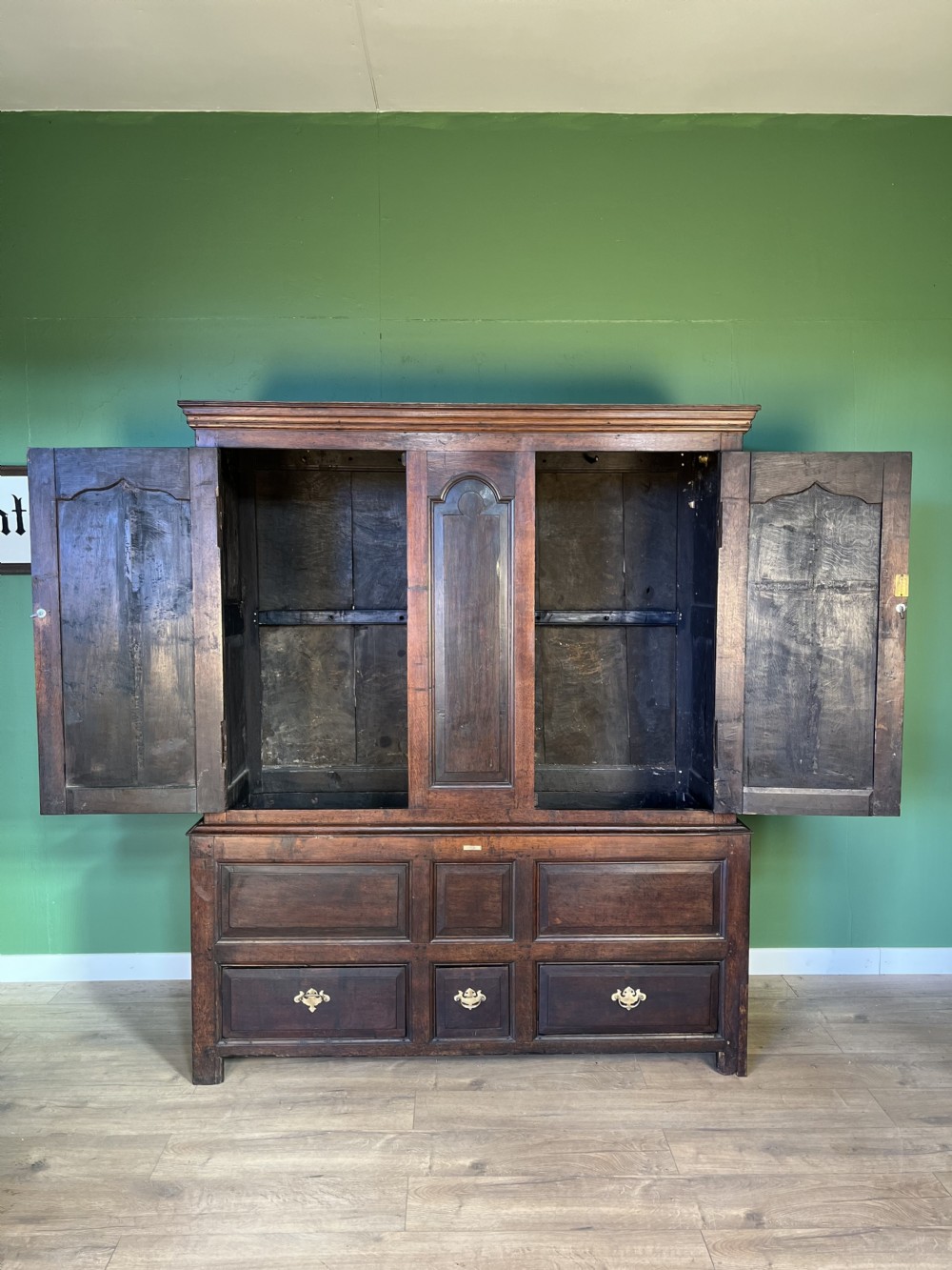 A mid-18th-century dark oak tack cupboard featuring arched panelled upper doors and a lower drawer section with brass handles. View III
