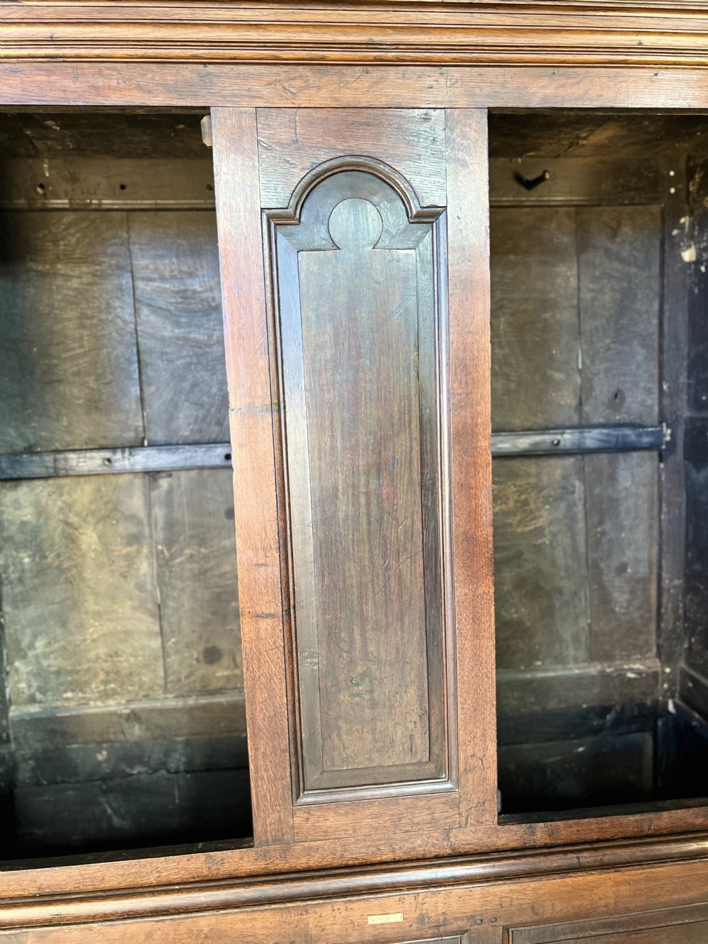A mid-18th-century dark oak tack cupboard featuring arched panelled upper doors and a lower drawer section with brass handles. View IV
