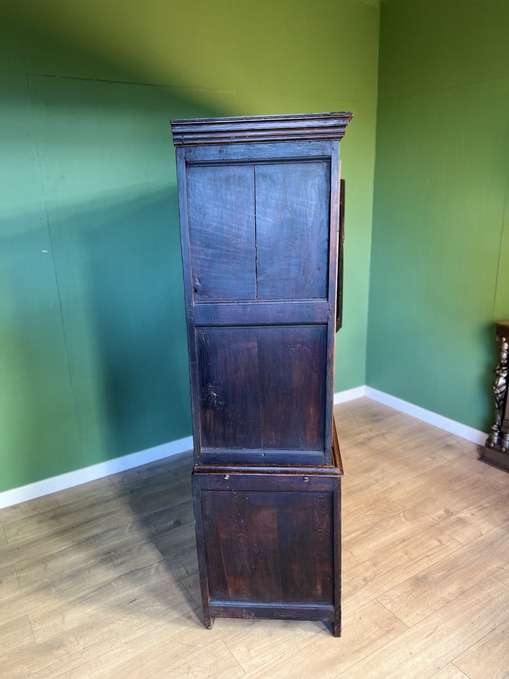 A mid-18th-century dark oak tack cupboard featuring arched panelled upper doors and a lower drawer section with brass handles. View VI