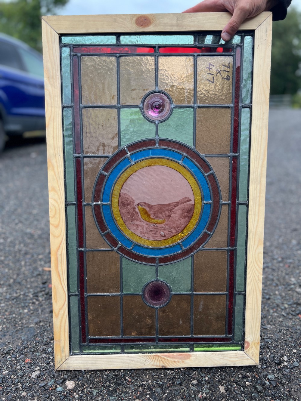 A rectangular Victorian leaded glass window panel featuring a central hand-painted bird roundel framed by colourful geometric borders and circular bullseye glass accents.