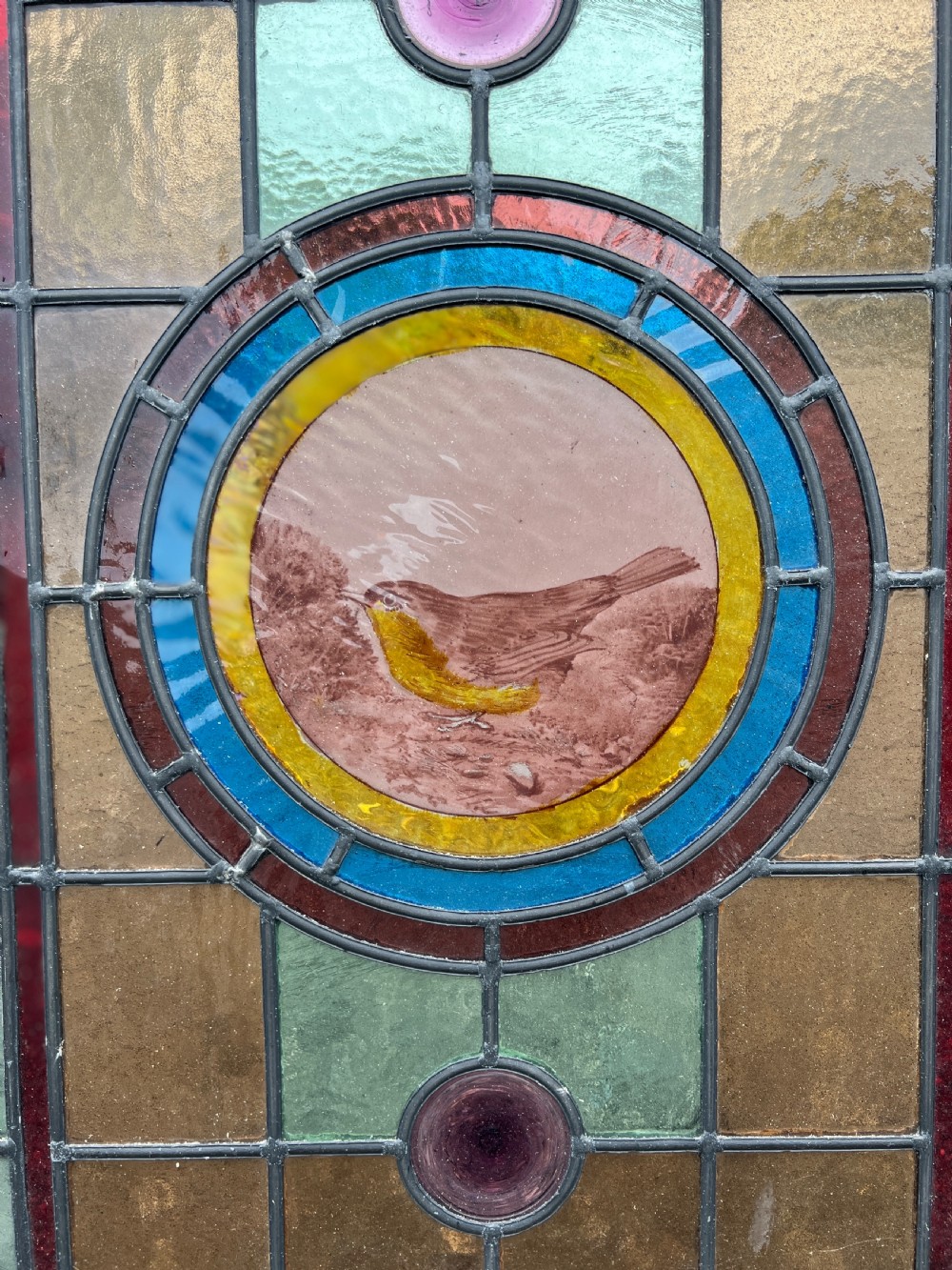 A rectangular Victorian leaded glass window panel featuring a central hand-painted bird roundel framed by colourful geometric borders and circular bullseye glass accents. View II