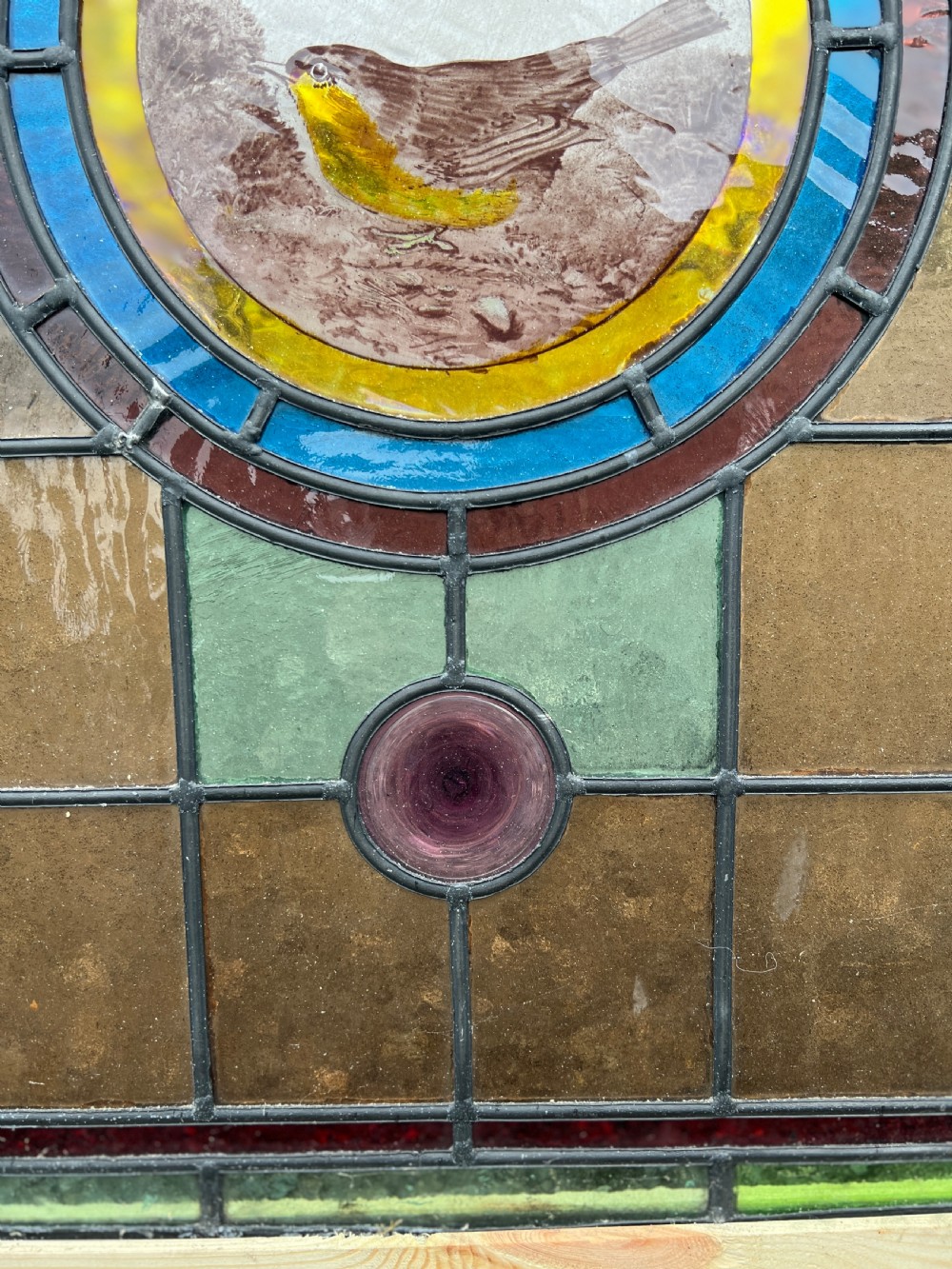A rectangular Victorian leaded glass window panel featuring a central hand-painted bird roundel framed by colourful geometric borders and circular bullseye glass accents. View V