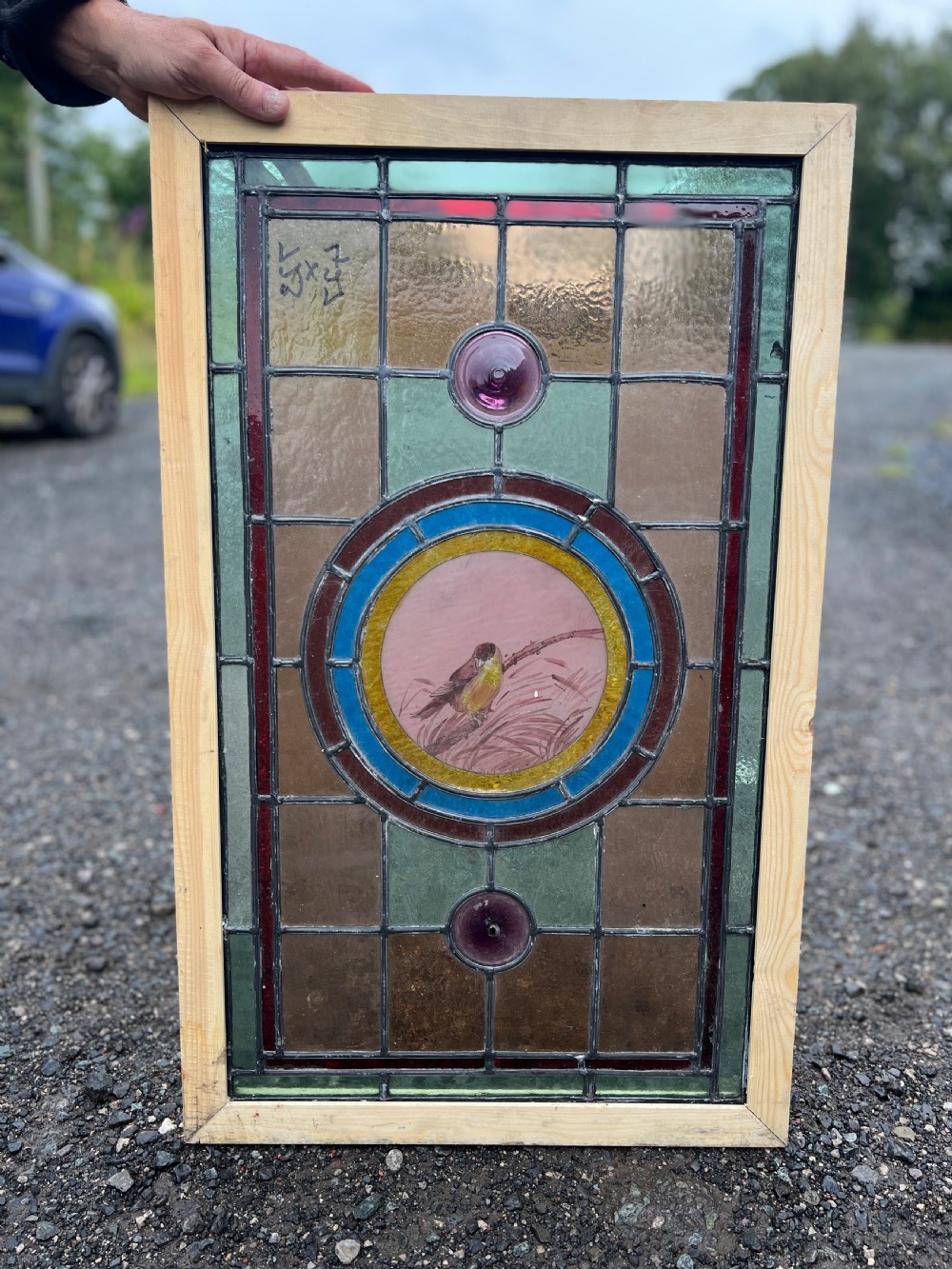 A rectangular Victorian stained glass panel featuring a hand-painted central medallion of a bird surrounded by geometric glass borders and purple roundels, housed in a pine frame.