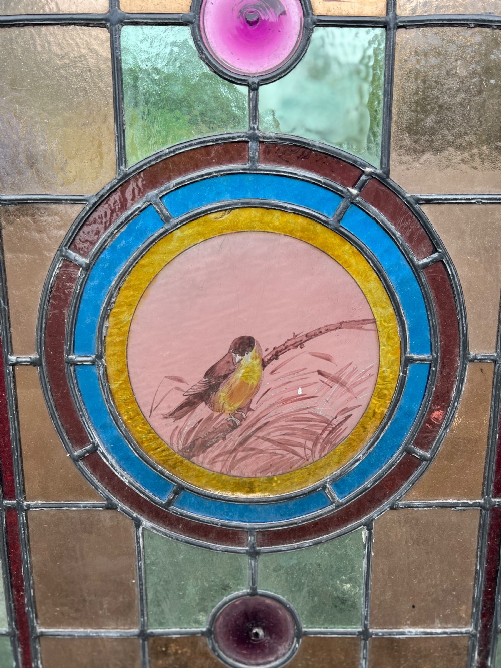 A rectangular Victorian stained glass panel featuring a hand-painted central medallion of a bird surrounded by geometric glass borders and purple roundels, housed in a pine frame. View II