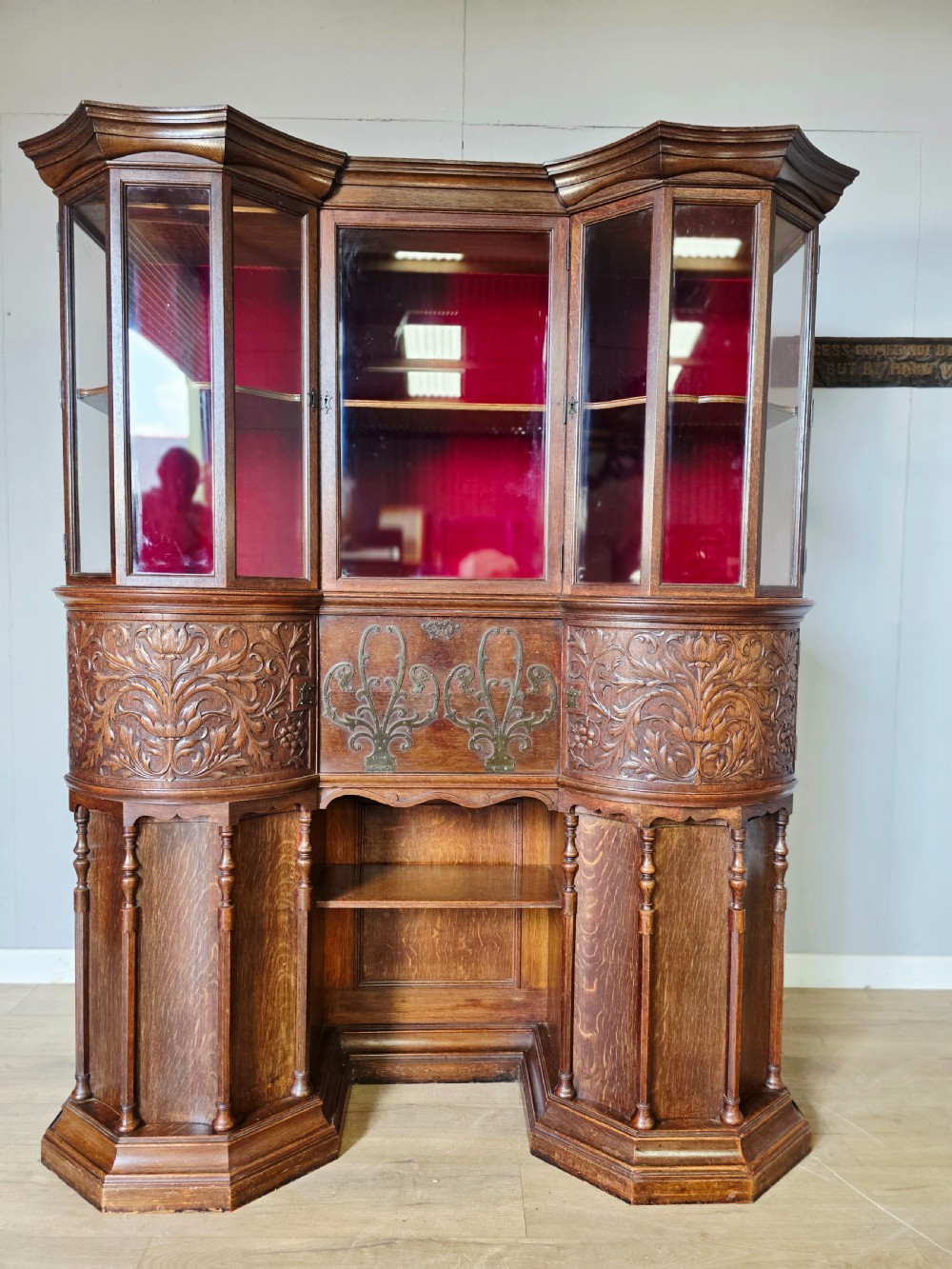 A late 19th-century carved oak cabinet desk with a red-lined glazed upper section, foliate carved lower panels, and brass strap hinges. View II