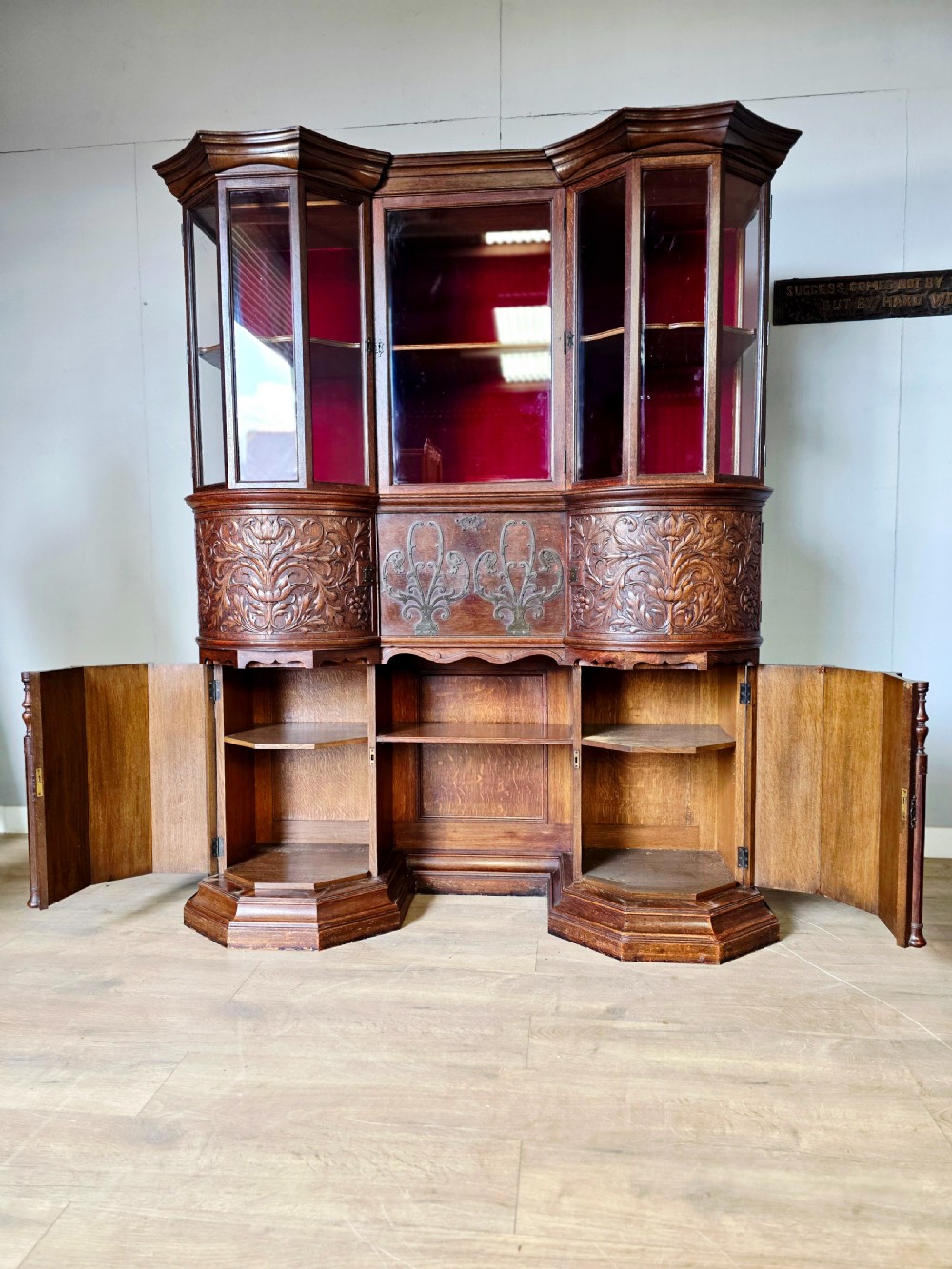 A late 19th-century carved oak cabinet desk with a red-lined glazed upper section, foliate carved lower panels, and brass strap hinges. View VII