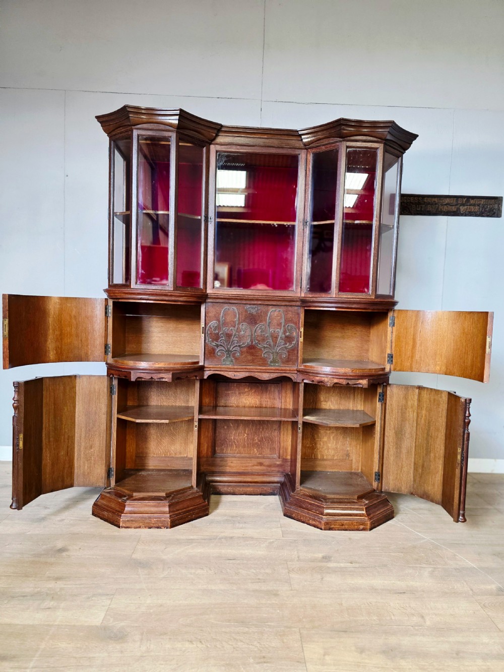 A late 19th-century carved oak cabinet desk with a red-lined glazed upper section, foliate carved lower panels, and brass strap hinges. View VIII