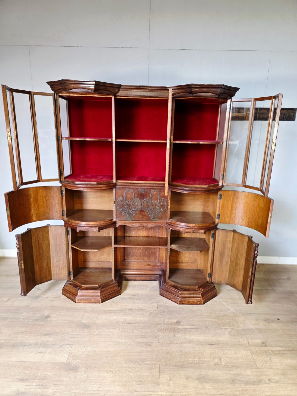 A late 19th-century carved oak cabinet desk with a red-lined glazed upper section, foliate carved lower panels, and brass strap hinges. View IX