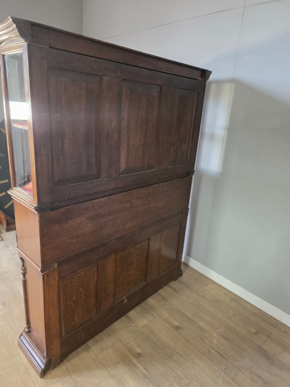 A late 19th-century carved oak cabinet desk with a red-lined glazed upper section, foliate carved lower panels, and brass strap hinges. View XIII