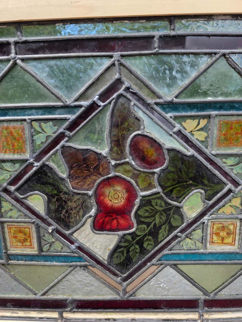 A rectangular late Victorian leaded glass window panel featuring central hand-painted floral motifs inside a geometric lead came frame with green and dark glass borders. View II