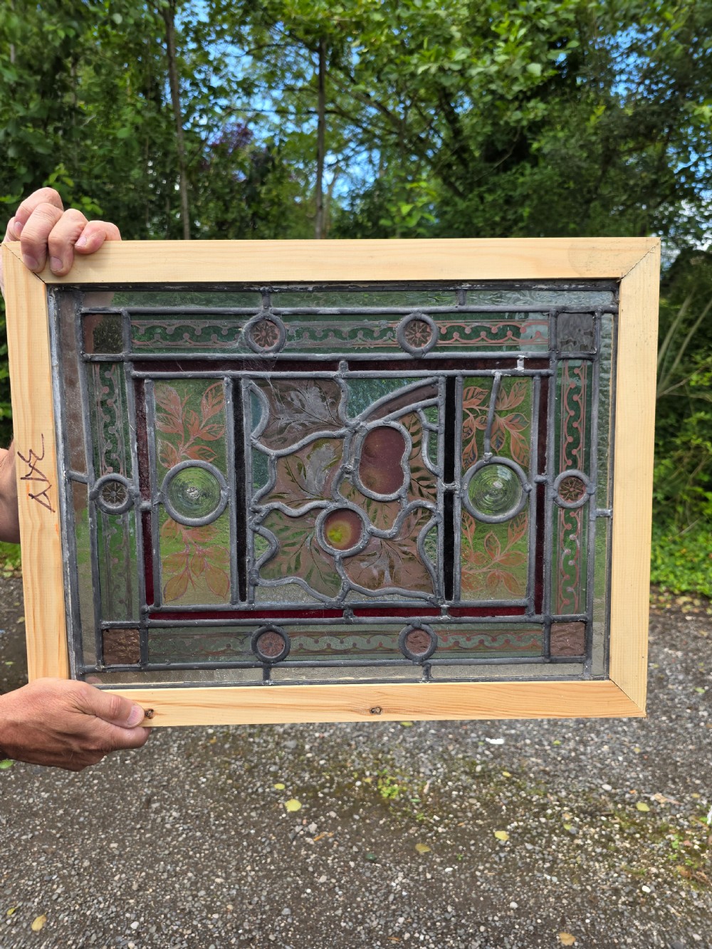 A rectangular Victorian leaded glass window panel featuring hand-painted fruit motifs and central bullseye glass inserts within a light wood frame.