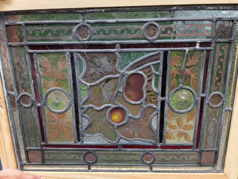 A rectangular Victorian leaded glass window panel featuring hand-painted fruit motifs and central bullseye glass inserts within a light wood frame. View II