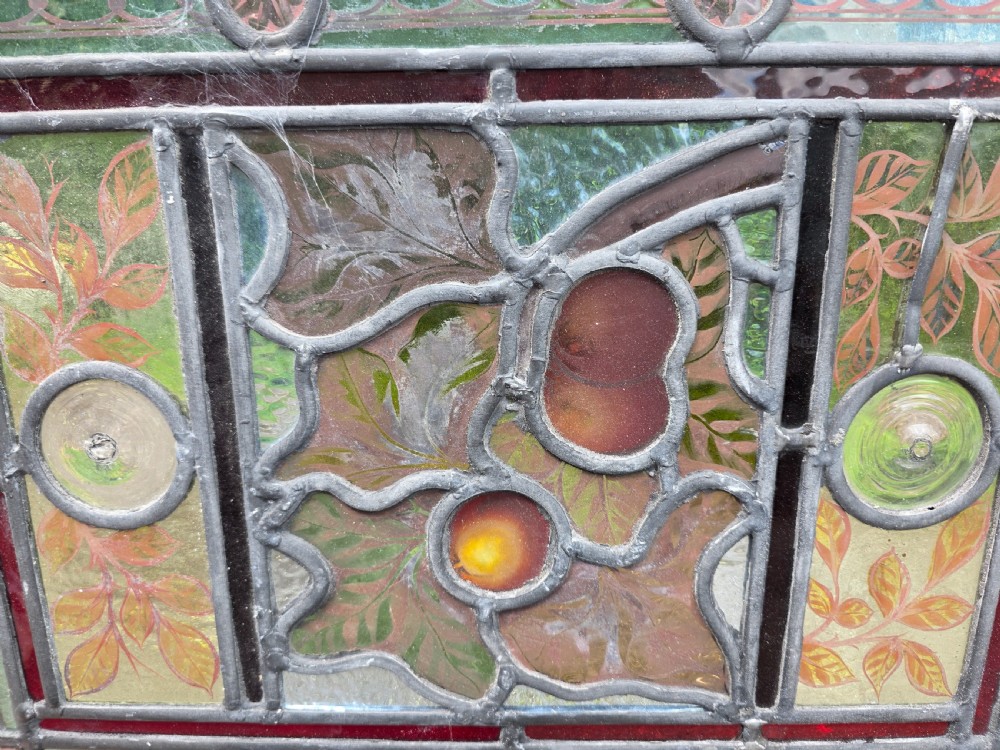 A rectangular Victorian leaded glass window panel featuring hand-painted fruit motifs and central bullseye glass inserts within a light wood frame. View III