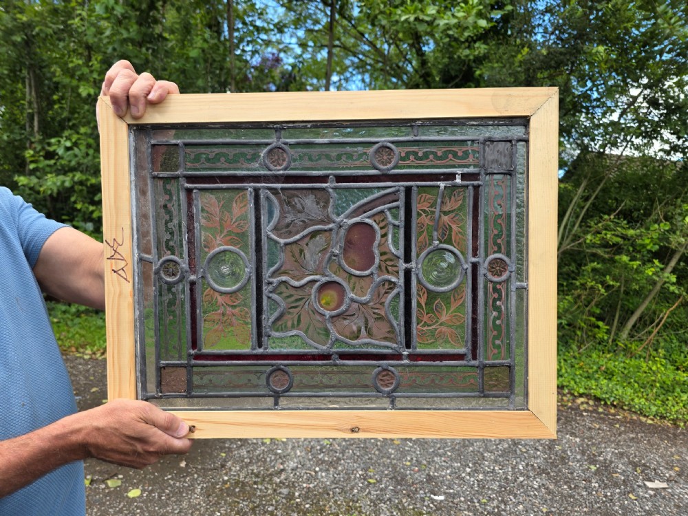 A rectangular Victorian leaded glass window panel featuring hand-painted fruit motifs and central bullseye glass inserts within a light wood frame. View IV