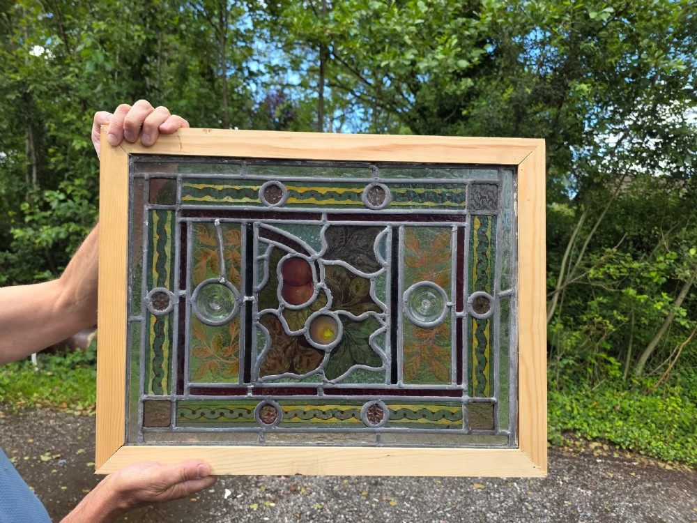 A rectangular Victorian leaded glass window panel featuring hand-painted fruit motifs and central bullseye glass inserts within a light wood frame. View V