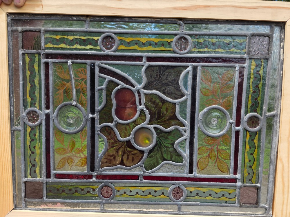 A rectangular Victorian leaded glass window panel featuring hand-painted fruit motifs and central bullseye glass inserts within a light wood frame. View VI