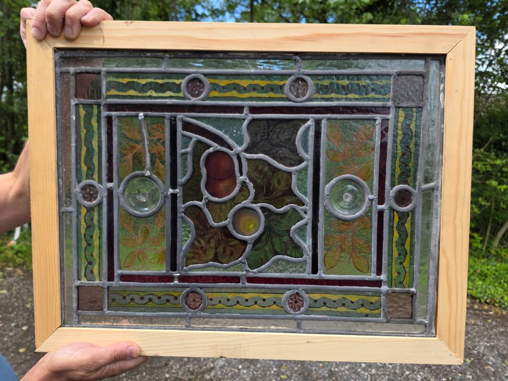 A rectangular Victorian leaded glass window panel featuring hand-painted fruit motifs and central bullseye glass inserts within a light wood frame. View VII