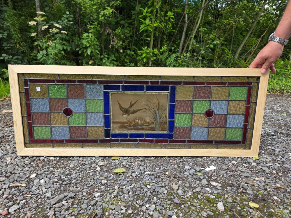 A rectangular antique leaded glass panel featuring a hand-painted central scene of a bird in flight over water lilies, surrounded by geometric colourful glass panes.