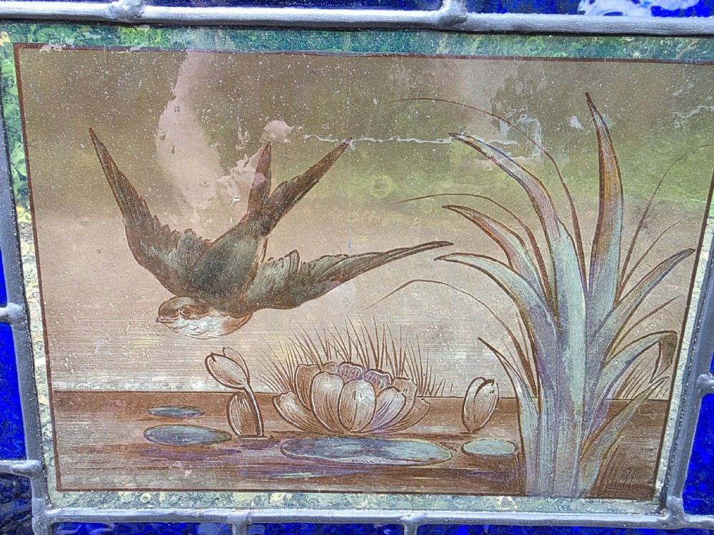 A rectangular antique leaded glass panel featuring a hand-painted central scene of a bird in flight over water lilies, surrounded by geometric colourful glass panes. View IV